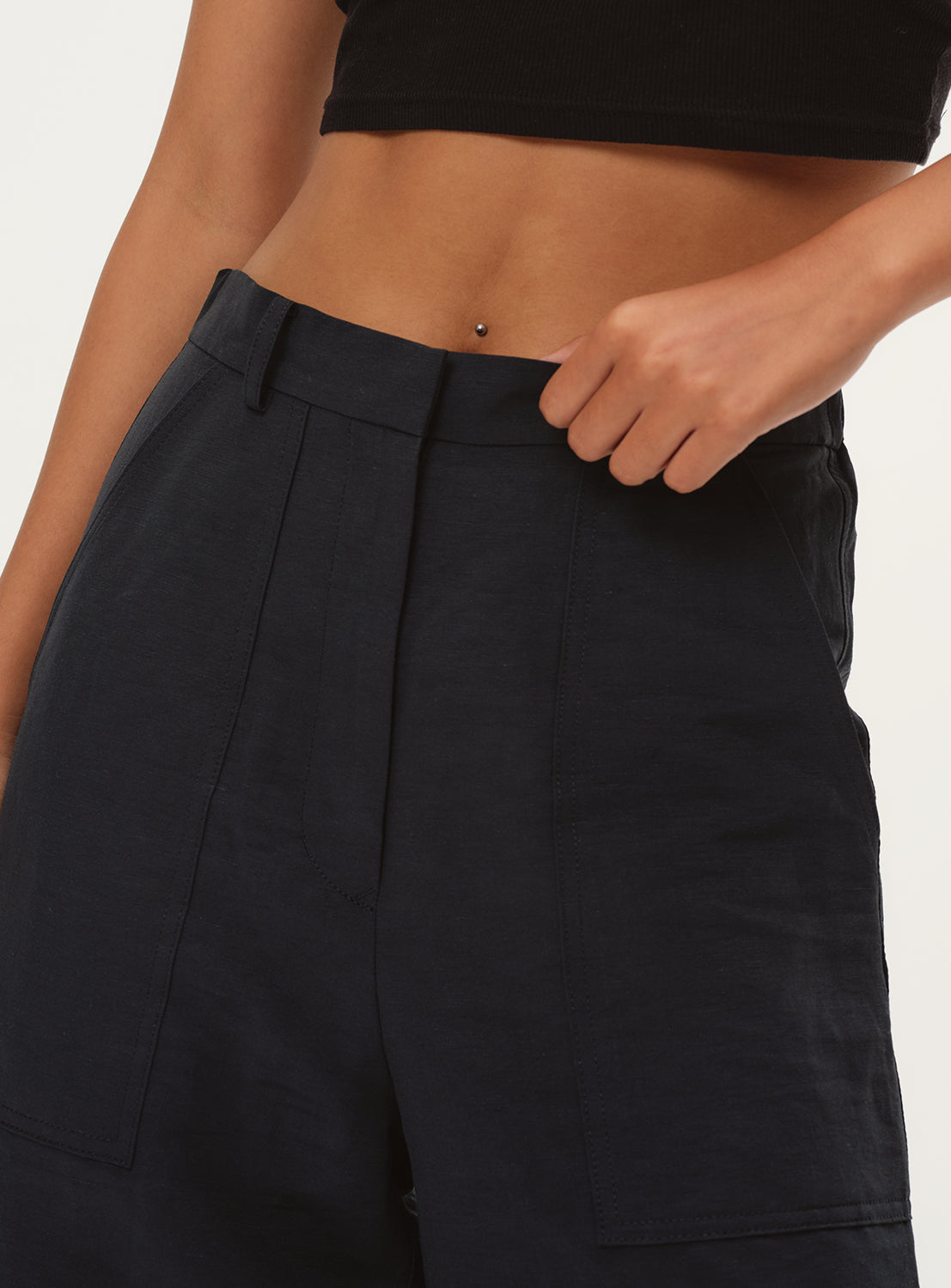 Close-up of a model's waist, highlighting the waistband and the fabric of the navy blue pants.