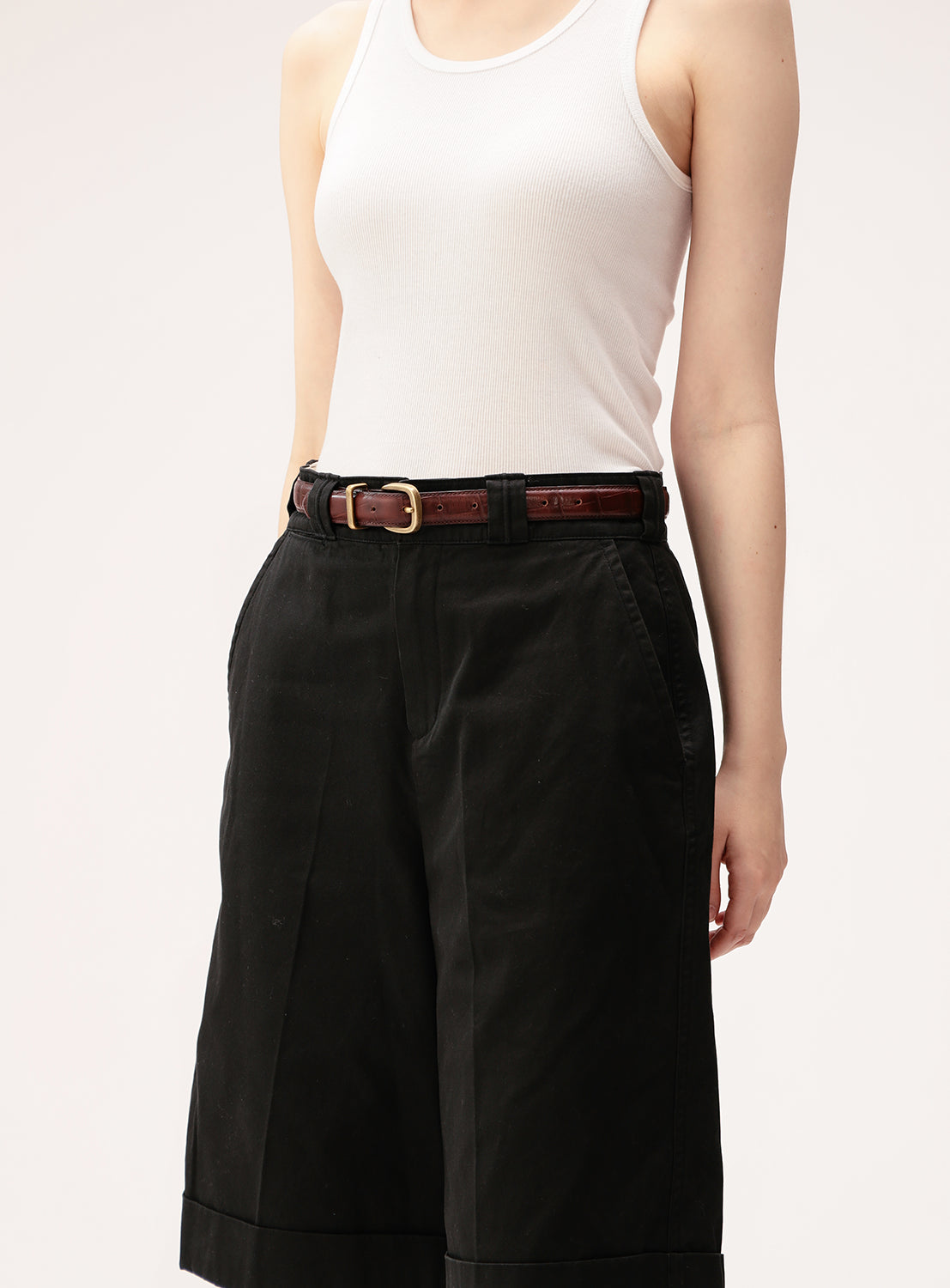 A person wearing a white ribbed tank top, black high-waisted wide-leg shorts, and the BEAMS BOY 25mm Crocodile Embossed Feather Leather Belt, featuring an antique gold buckle, stands with hands in pockets, shown from shoulders to knees.