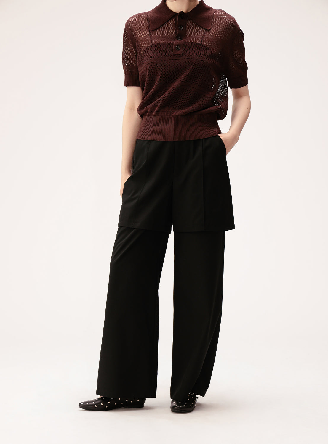A person wearing a short-sleeved maroon knit top, Ray BEAMS Half Layered Wide-Leg Trousers in black crafted from lightweight suiting fabric, and black shoes with silver studs. Their hands are in their pockets, and their head is not visible in the image.