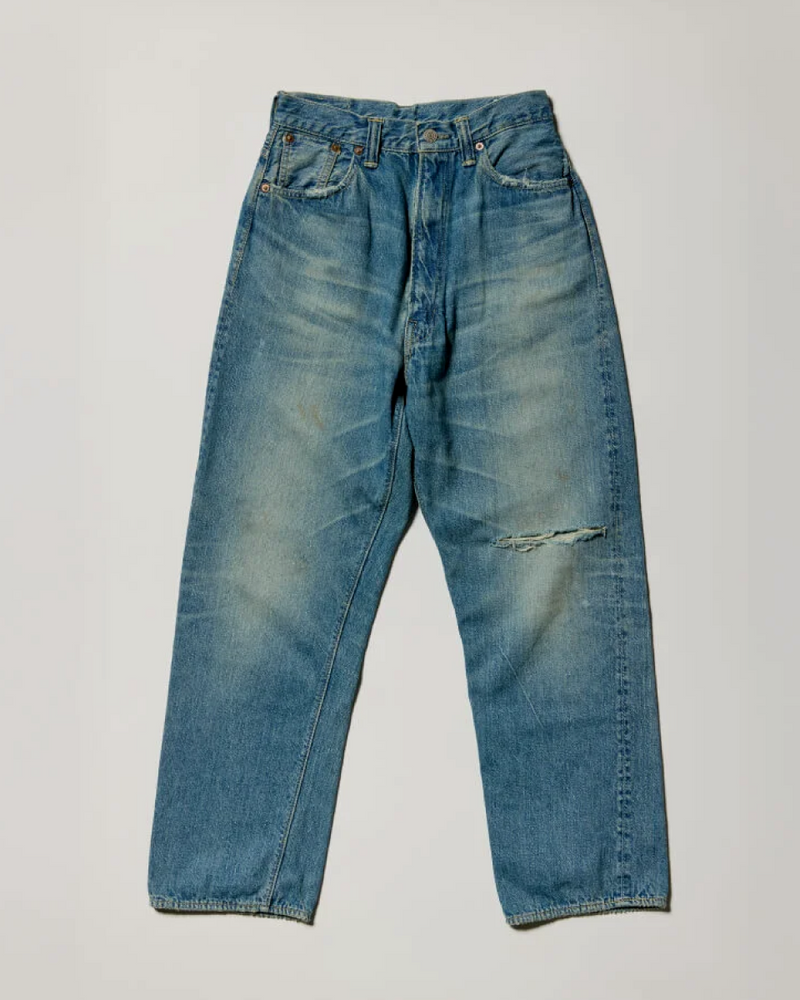 A pair of faded blue jeans with a slight rip on the right thigh, laid flat on a neutral background.