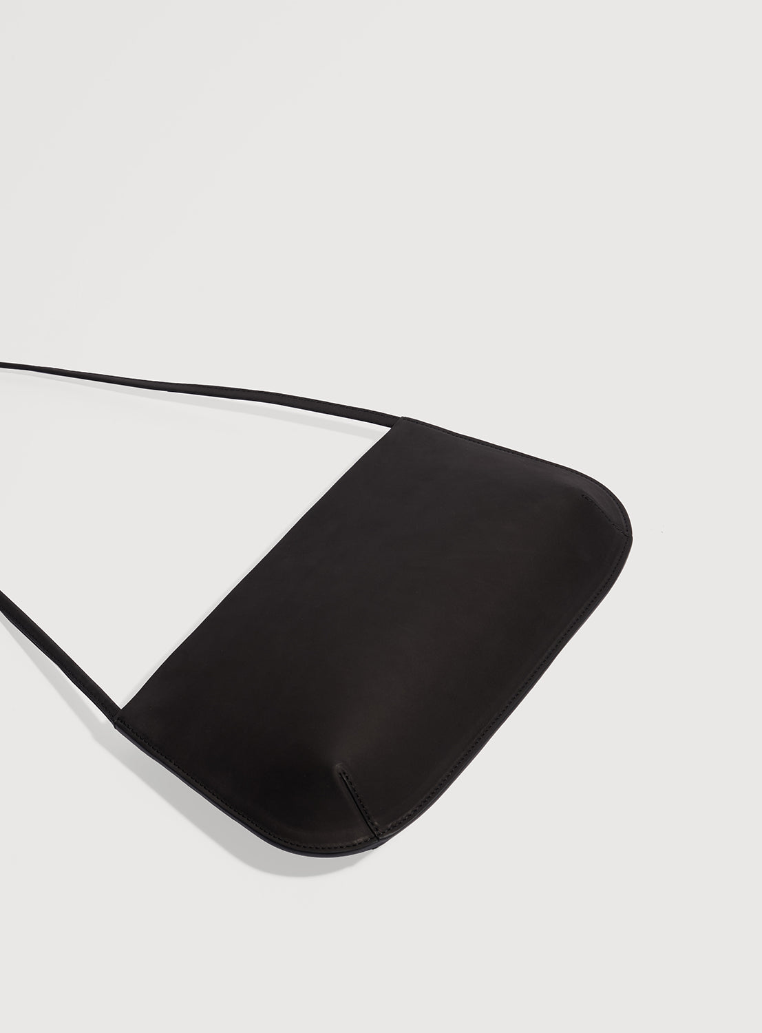 Black ultra-slim, curved silhouette shoulder bag laid flat. 