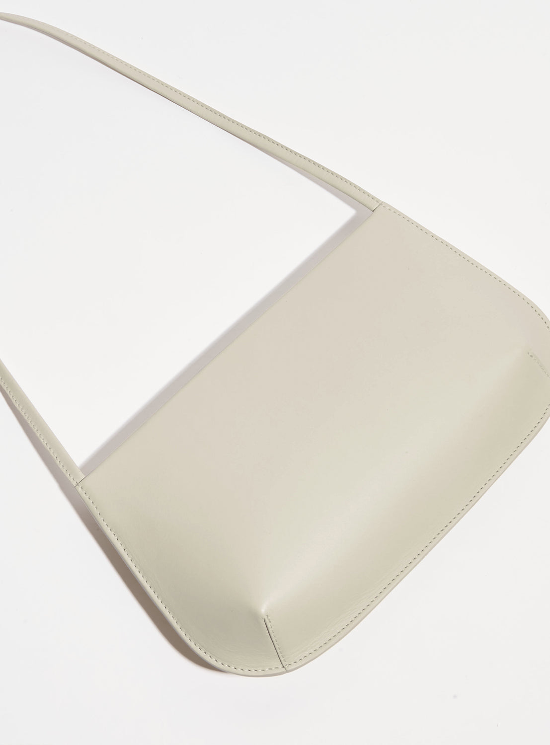 Beige ultra-slim, curved silhouette shoulder bag laid flat. 