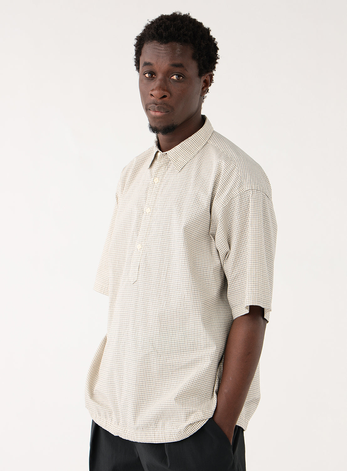 Model wearing an off-white check-patterned pullover shirt, front view, highlighting the relaxed silhouette and neat neckline.