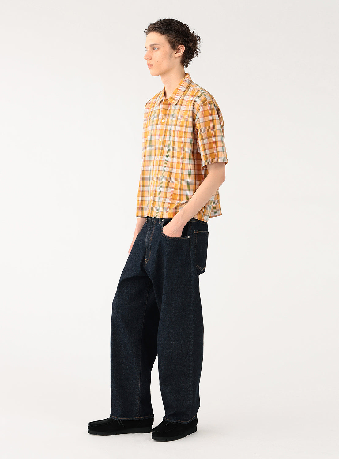 Model wearing an orange with green and orange striped cropped-length check shirt, side view, emphasizing the relaxed silhouette.