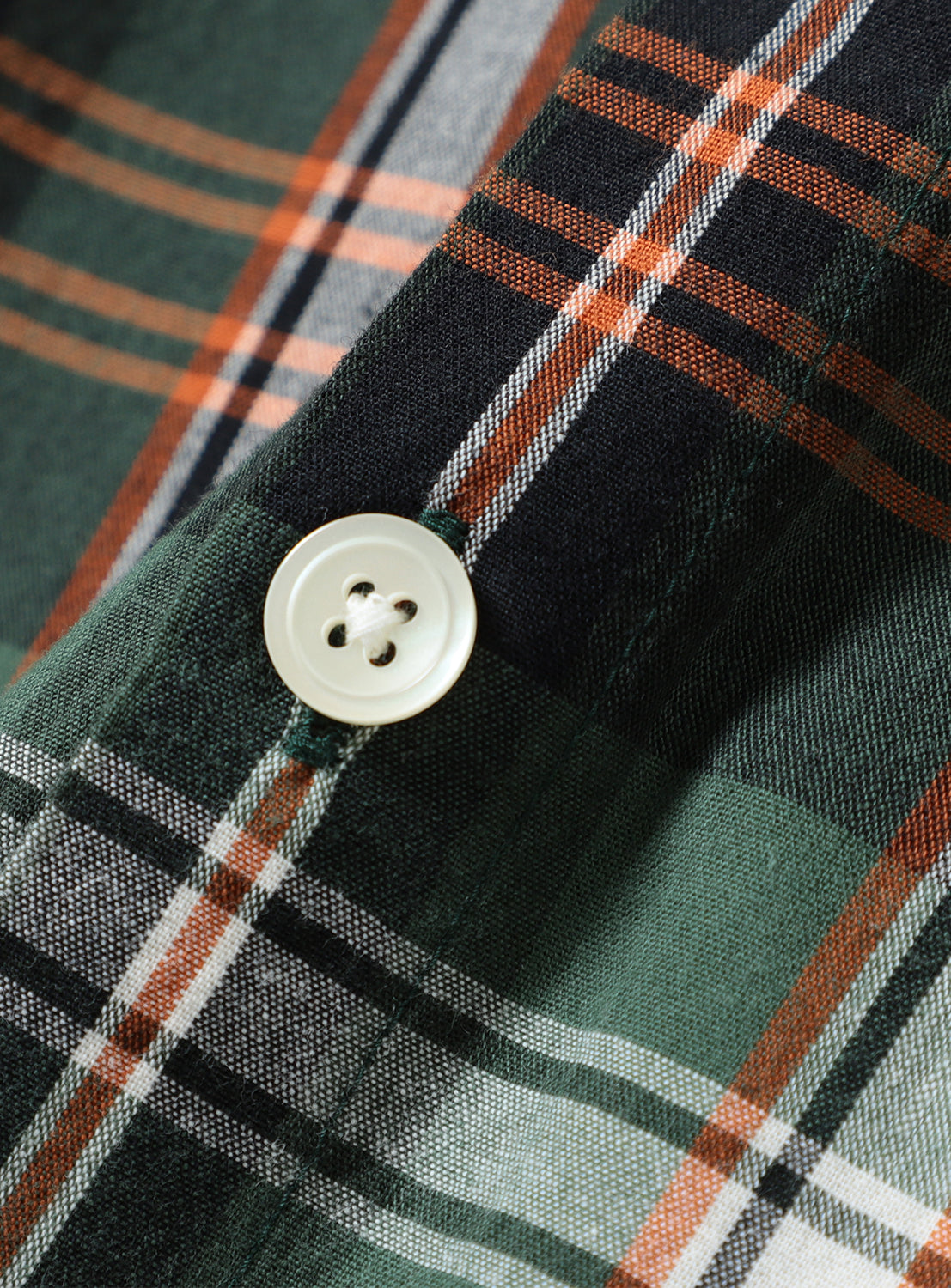 Close-up of green and orange plaid check shirt fabric and button, detailing the breathable cotton texture.
