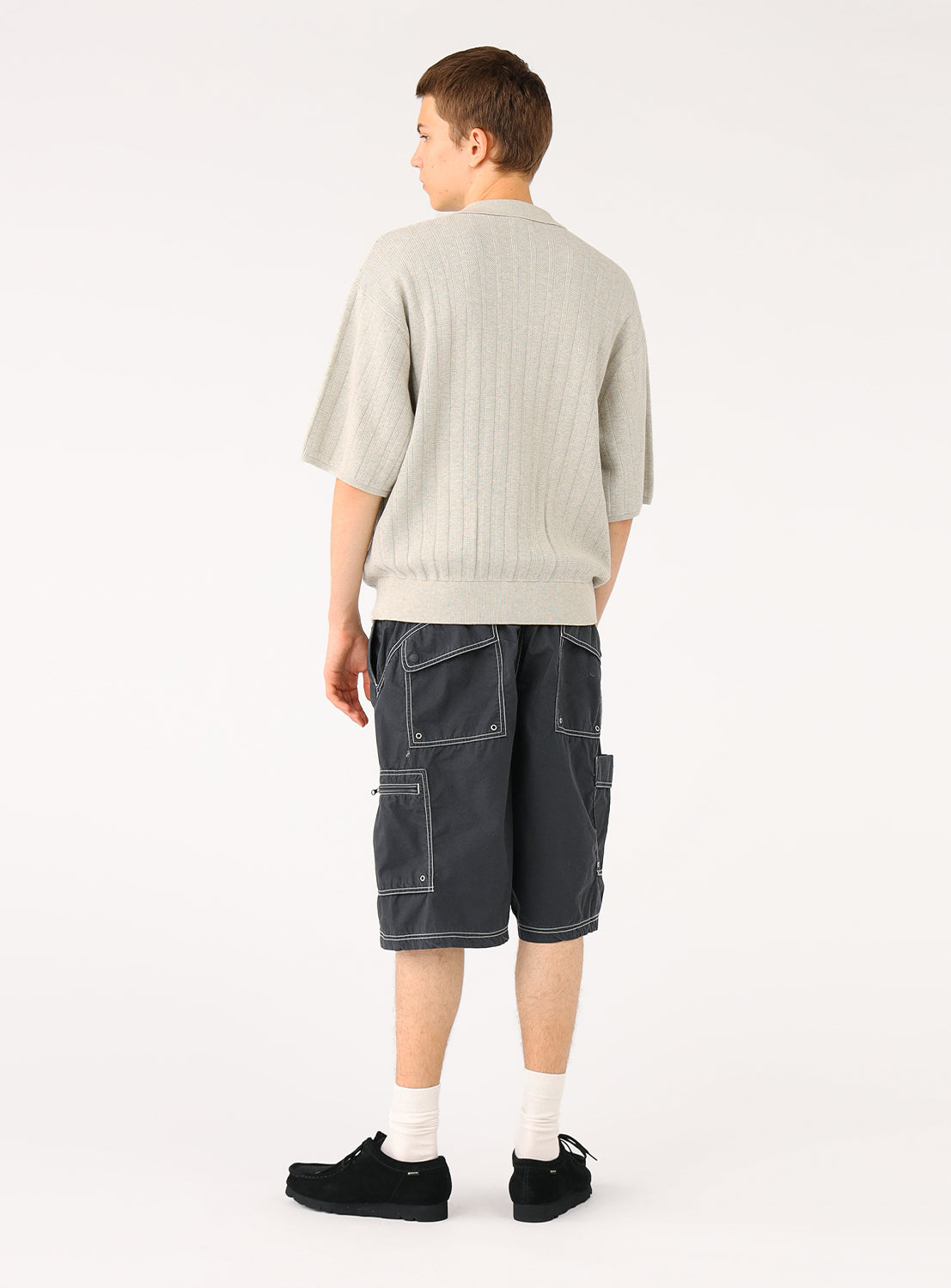 Male model from behind in light grey knit polo and dark shorts, showing back of shirt.