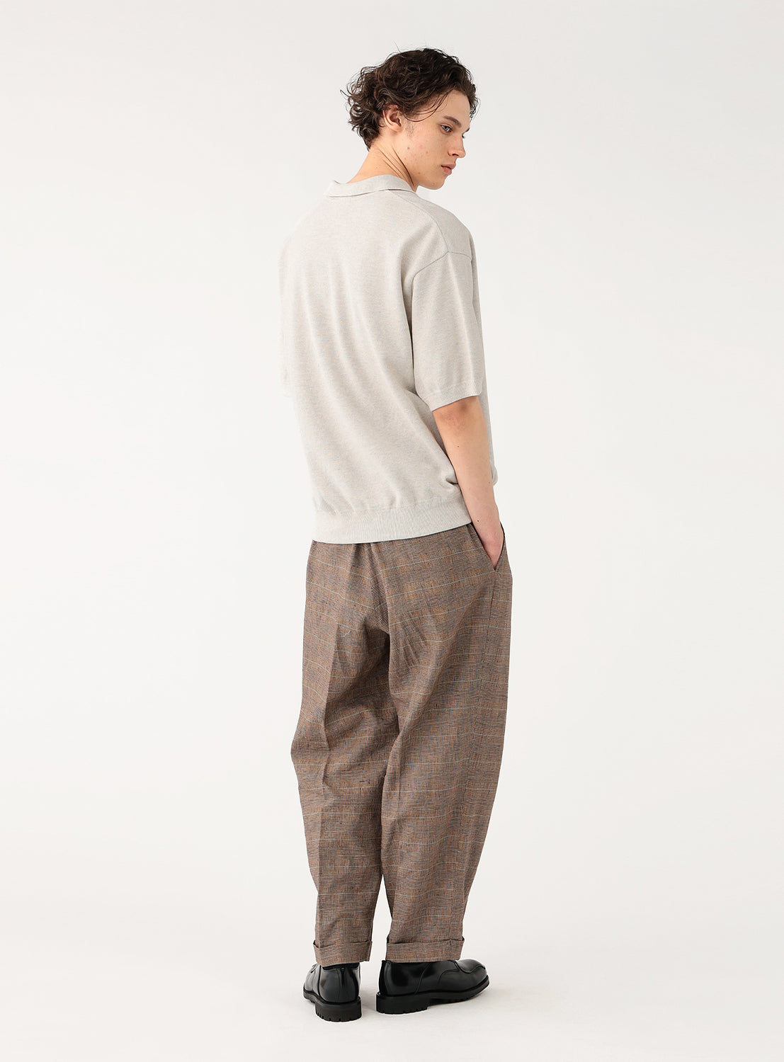 Male model in light beige knit polo standing casually, back full body view.