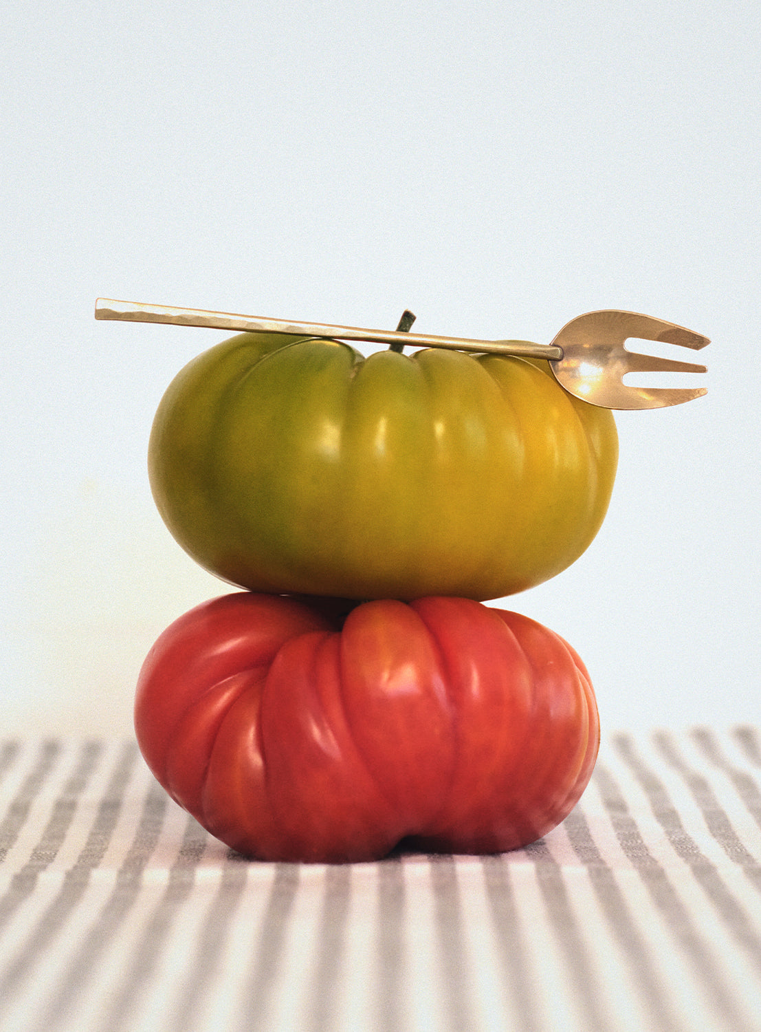 Two stacked tomatoes with a gold fork on top.