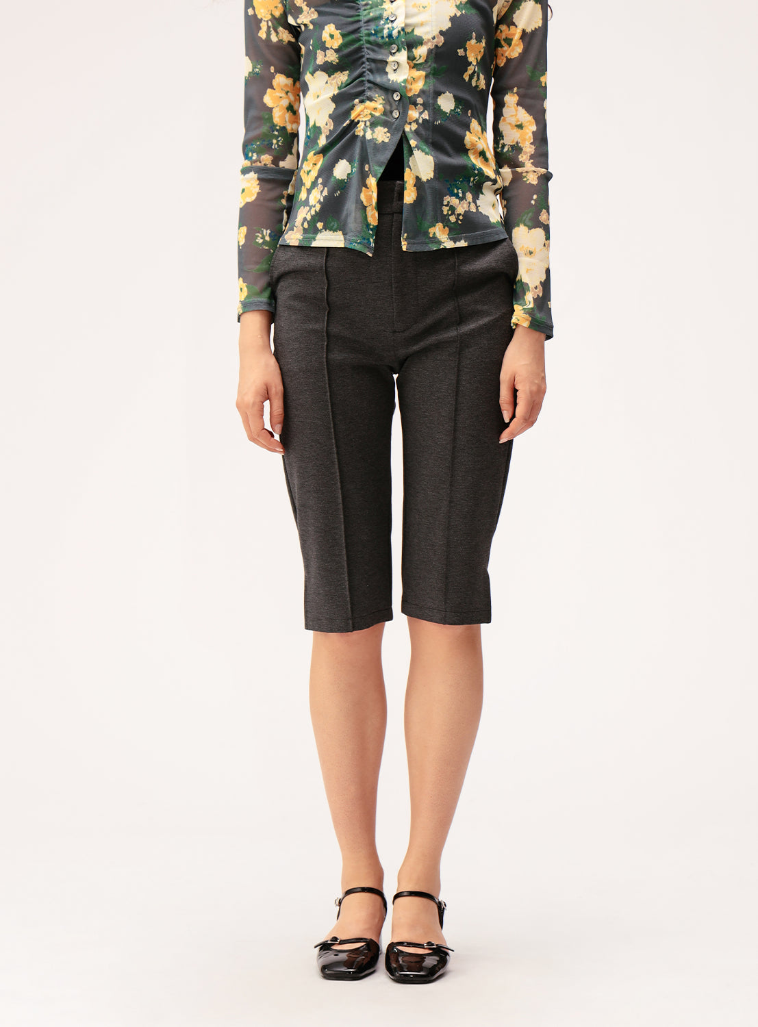A person wearing Ray BEAMS' Stretch Capri Pants, paired with a floral long-sleeve sheer blouse and black flat shoes, stands against a plain white background, creating a slim silhouette.