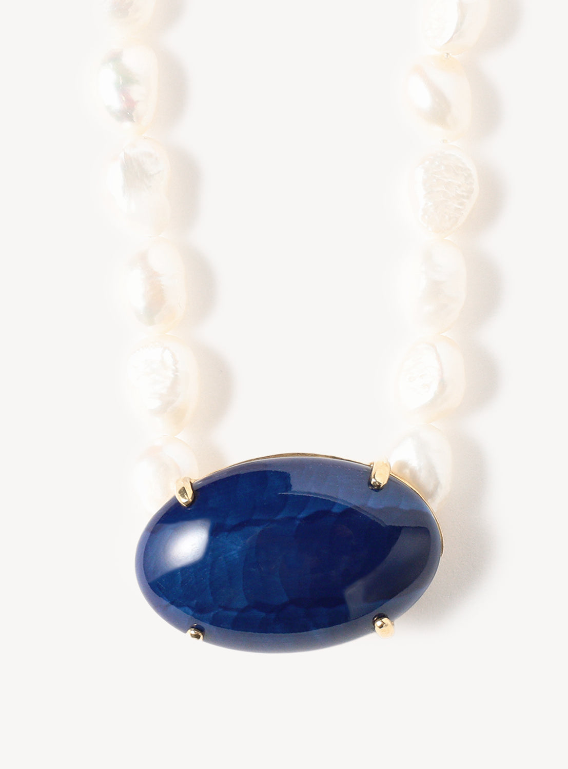 A close-up of the Hizen Jewelry Arita Ware Motif and Pearl Long Necklace, featuring irregular freshwater pearls and a large oval-shaped blue Arita ware centerpiece set in a gold frame.