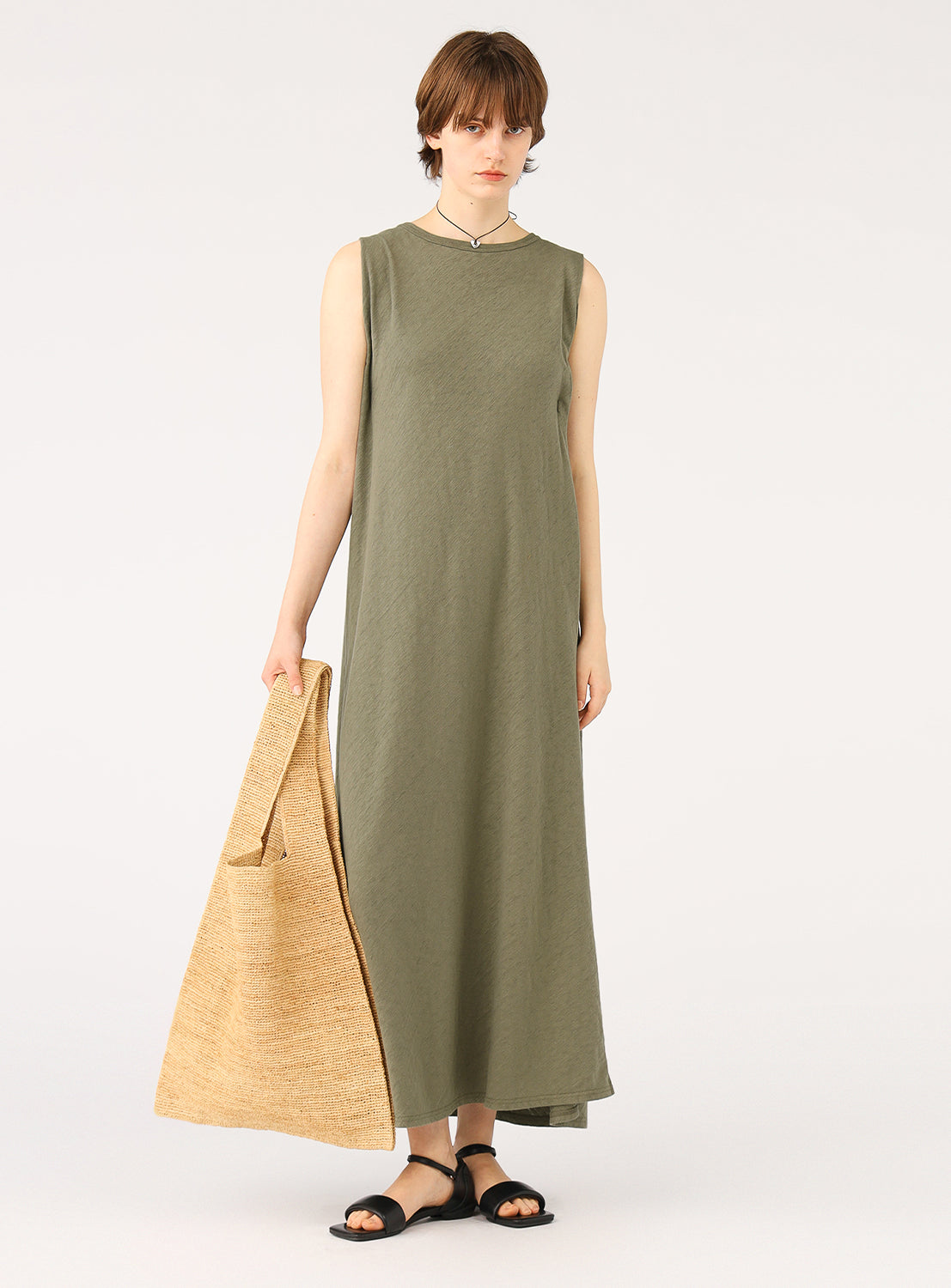 Model wearing a relaxed fit olive green maxi dress, styled with sandals and a woven tote bag.