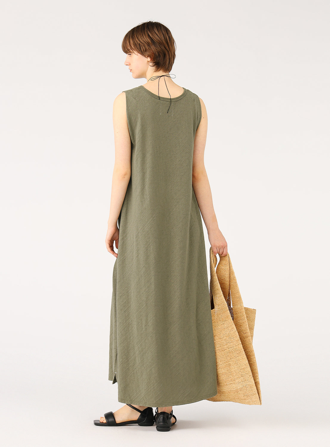 Back view of a model wearing an olive green maxi dress, holding a tote bag and highlighting the simple, clean design.