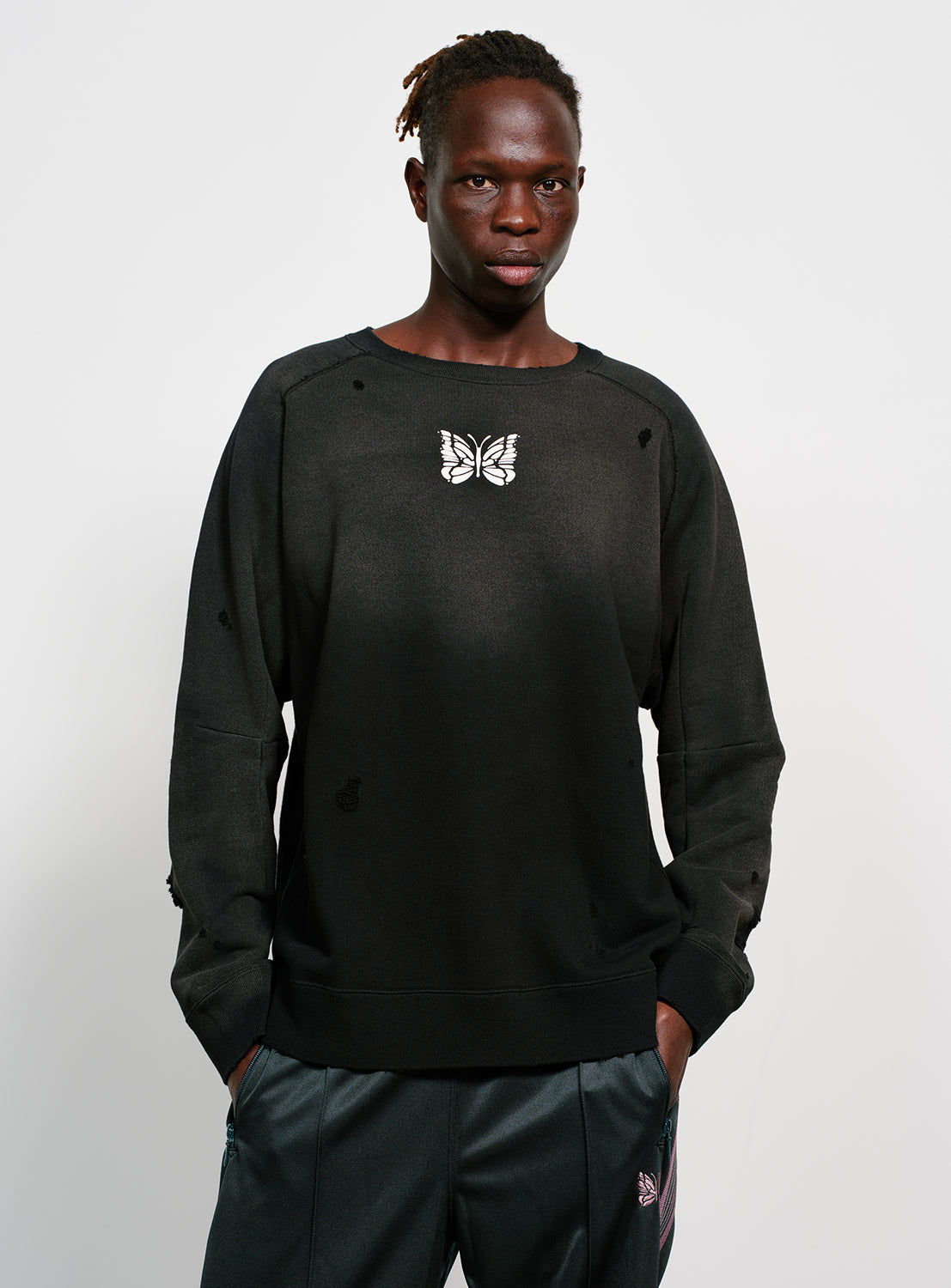 Model wearing a black distressed and faded sweatshirt with a butterfly design in white. 