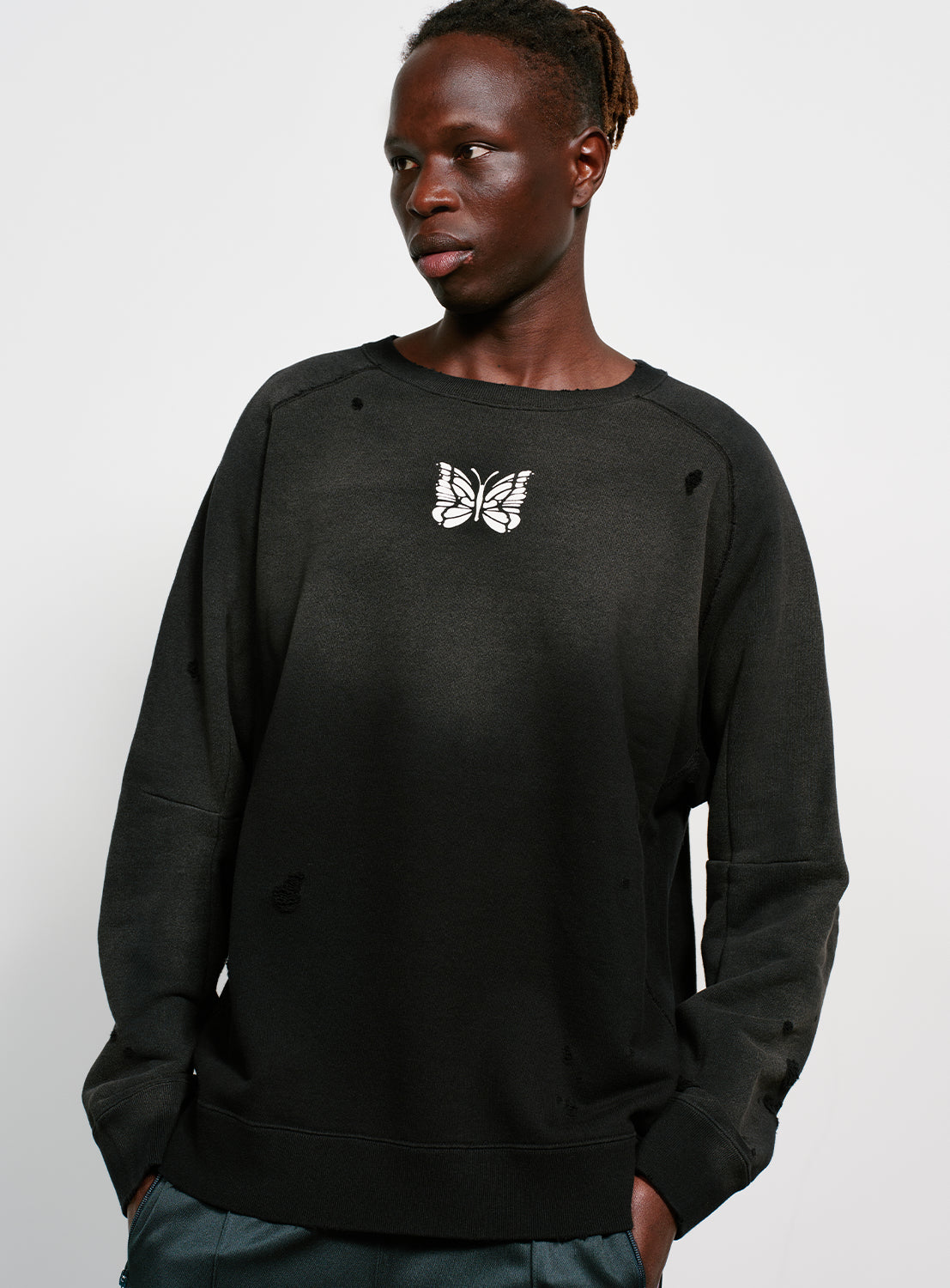 Model wearing a black distressed and faded sweatshirt with a butterfly design in white. 