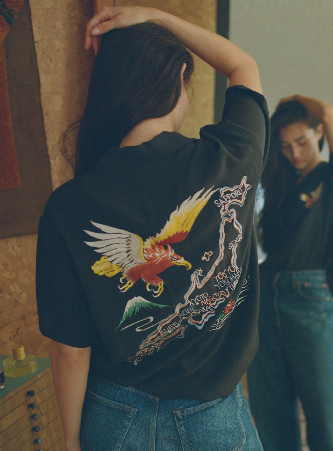 Model wearing a black button down shirt with an eagle, a map of Japan and a dragon embroidered on the back.
