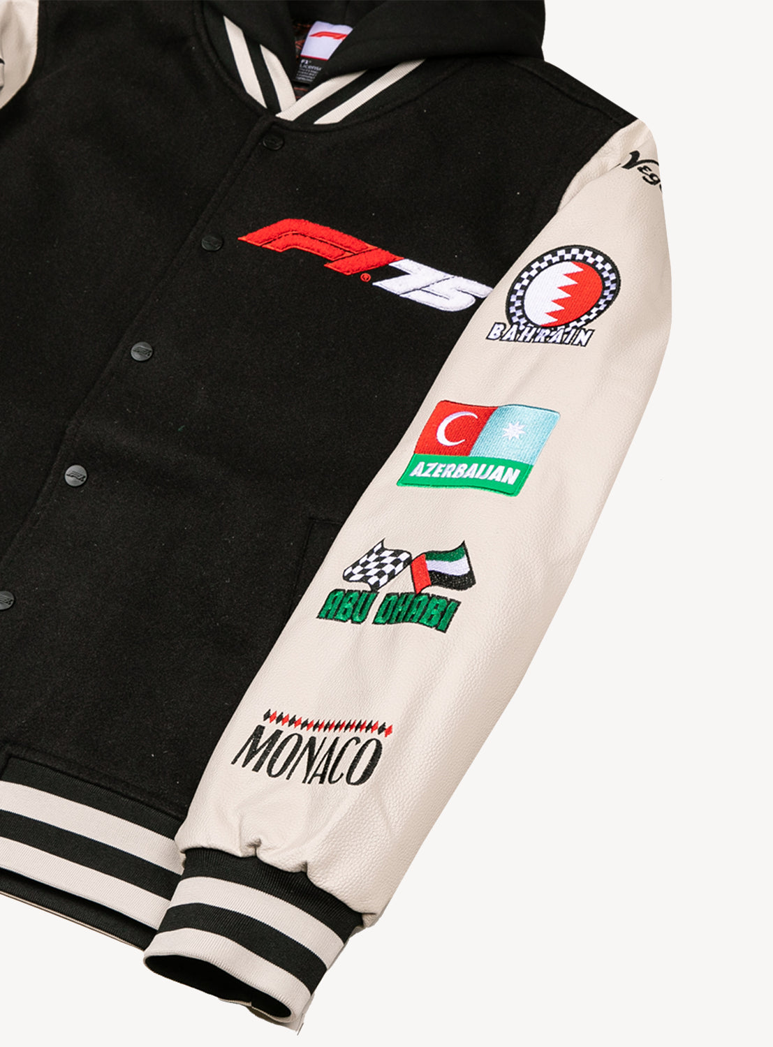 Close up of black button down varsity hooded jacket with white sleeves and racing locations going down the sleeves and the F1 75 logo on the chest. 