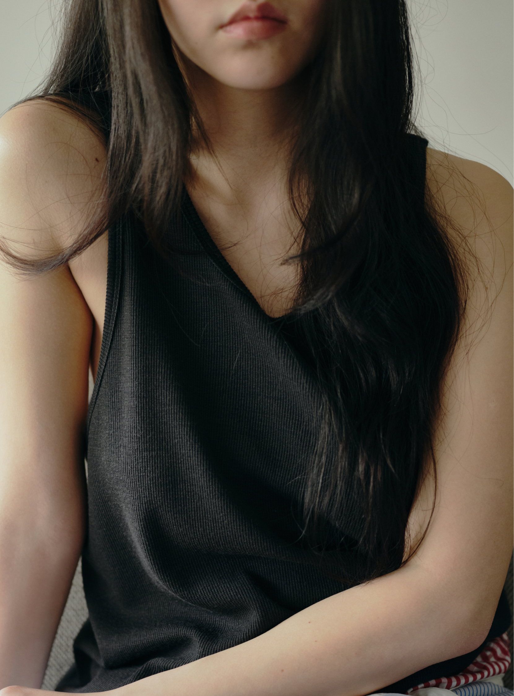 A woman with long dark hair wears the A - Washable Ribbed Wool Tank Top by BEAMS, sitting with relaxed arms and a calm expression against a neutral background.