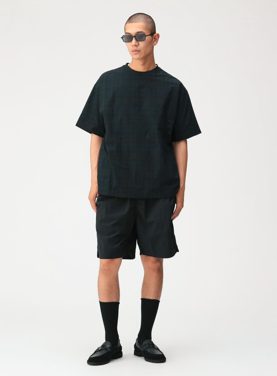 A person wearing dark sunglasses, matching shorts, black socks, and black shoes stands against a plain white background, dressed in a BEAMS Relaxed Fit Dynamic Dry Crew Neck T-Shirt.