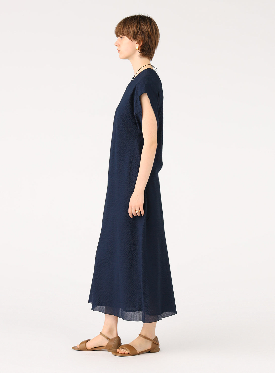 Female model wearing a full-length navy blue dress with short sleeves, standing in a side profile.