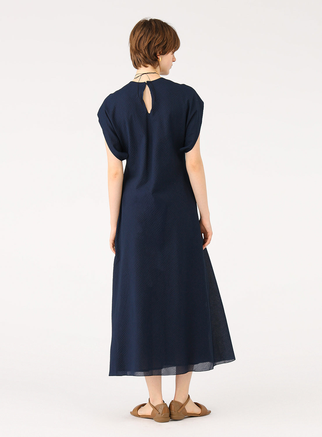Female model from behind, wearing a full-length navy blue dress with a back slit or opening at the neck.
