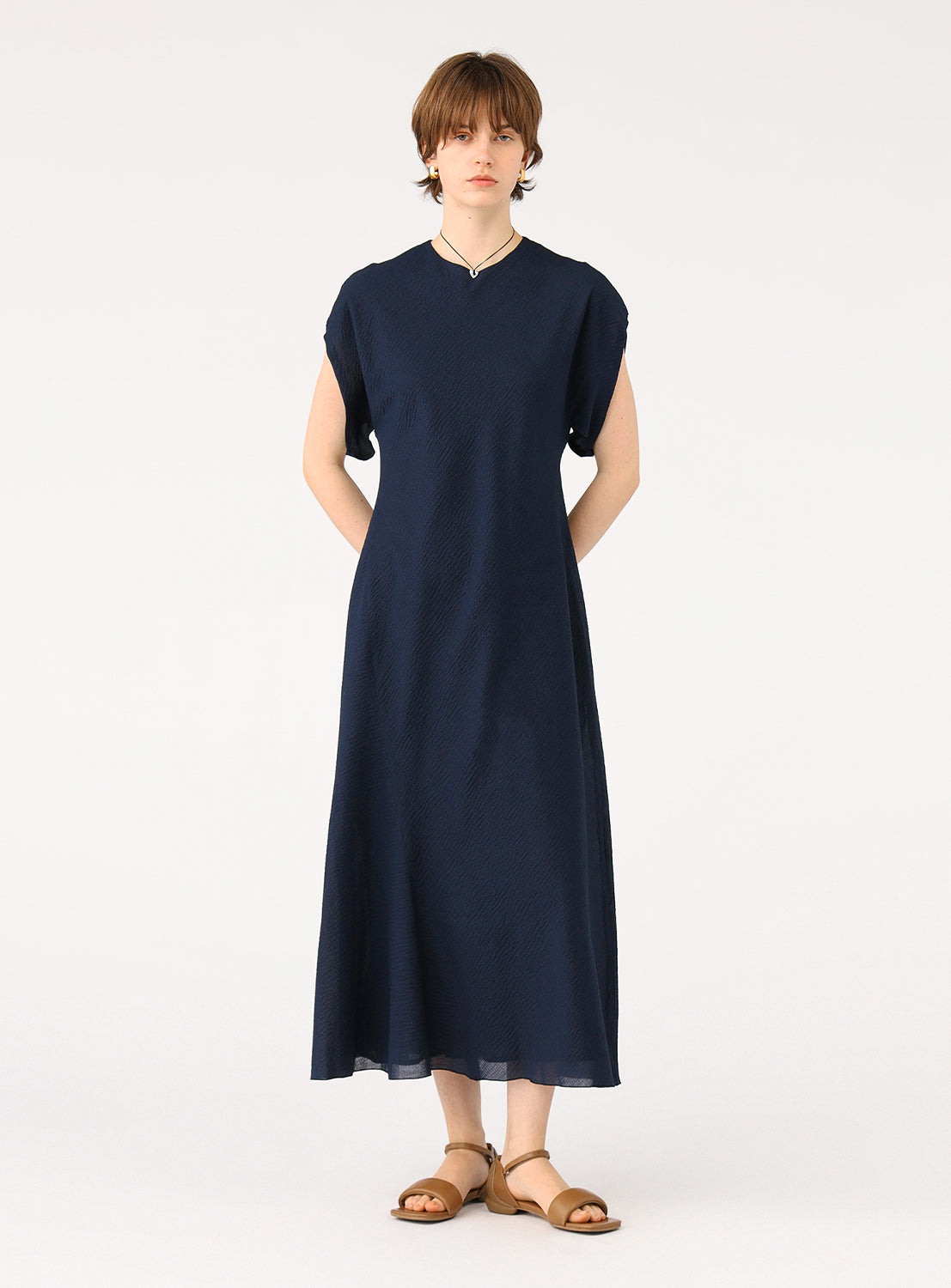 Female model wearing a full-length navy blue dress with short sleeves, standing facing forward.