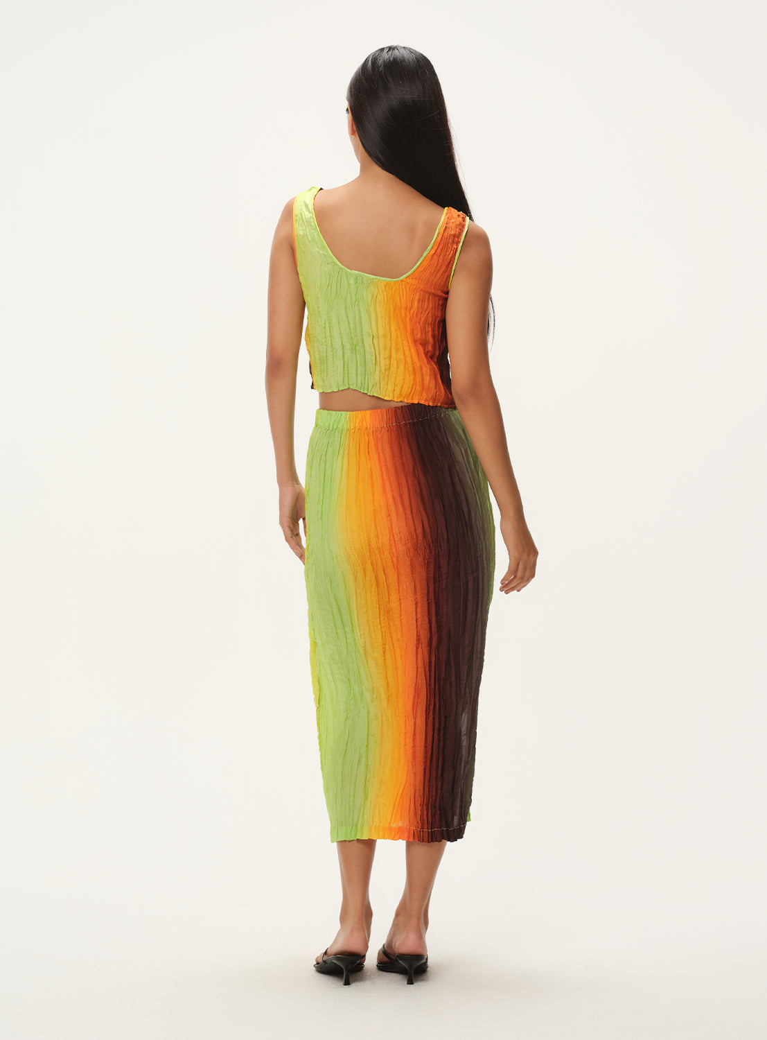 A rear-facing view of a woman wearing a vertically striped knit midi skirt and a matching sleeveless top, standing.