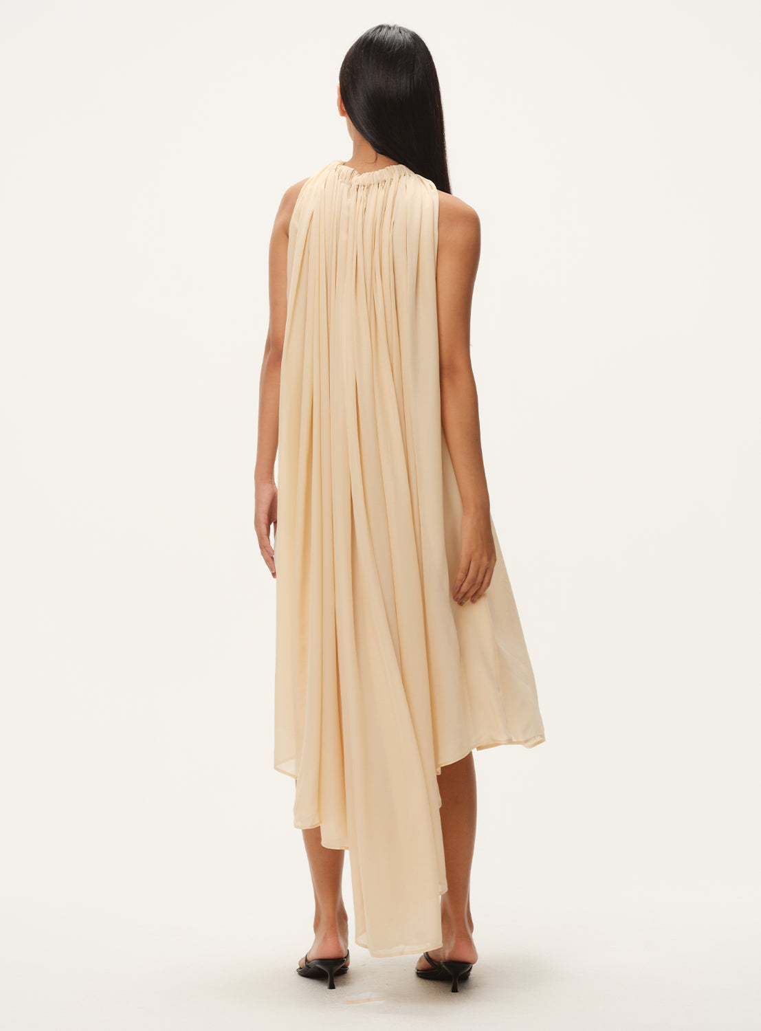 Back if beige flowy silk dress with a draped design.