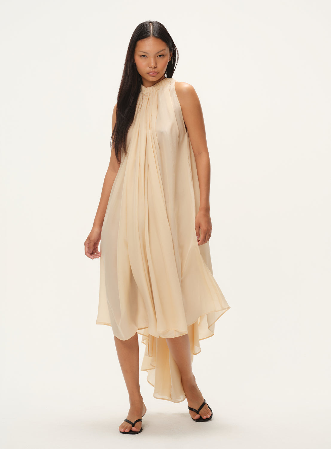 Model wearing a beige flowy silk dress with a high-low design. 