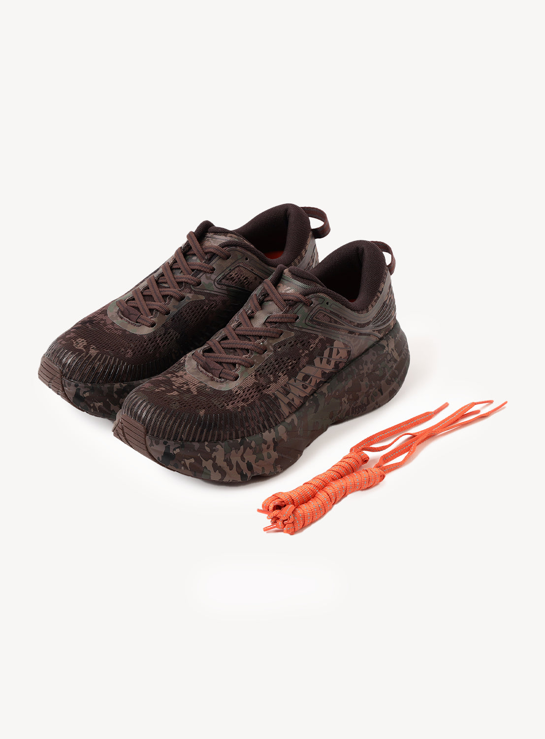 A pair of Hoka U BONDI 7 BEAMS sneakers in a dark camo pattern with black soles, positioned side by side. Designed with an engineered mesh upper for breathability, these shoes are displayed on a white background alongside an extra set of bright orange shoelaces.