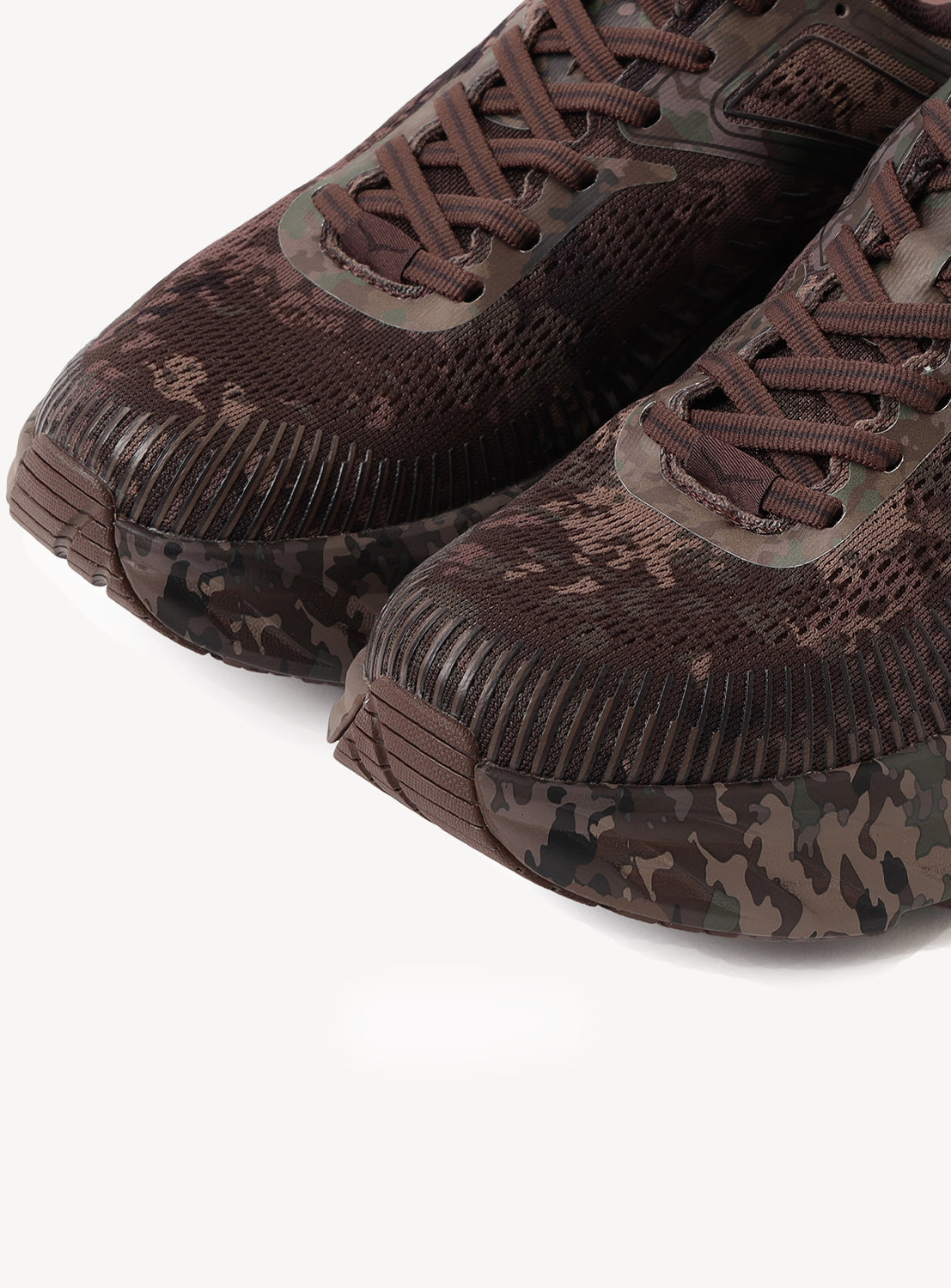 Close-up of two brown Hoka U BONDI 7 BEAMS sneakers featuring a camouflage pattern, emphasizing the engineered mesh upper, textured toe sections, laces, and part of the rubber outsole against a white background.