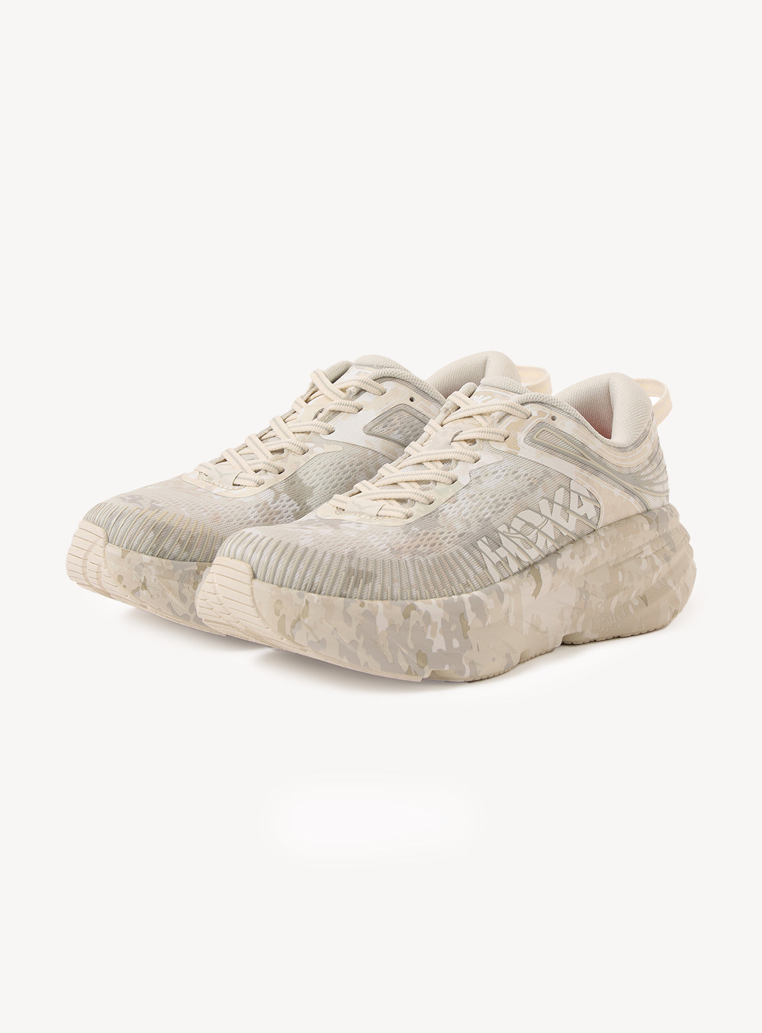 A pair of Hoka U BONDI 7 BEAMS sneakers in beige and off-white, showcasing a tonal camouflage pattern and thick, translucent soles. The engineered mesh upper enhances breathability and adds a modern touch. The shoes are displayed on a white background.