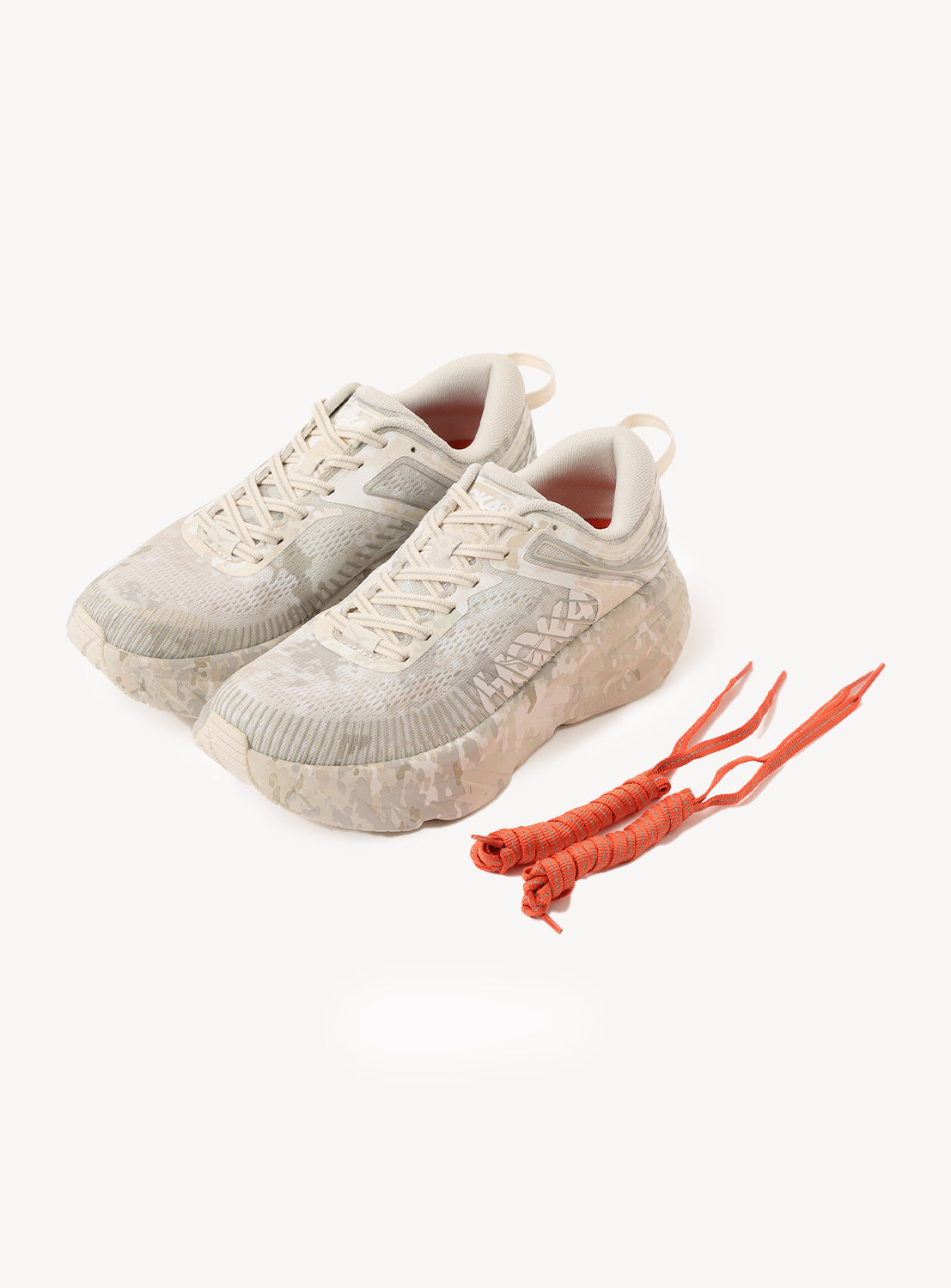 A pair of Hoka U BONDI 7 BEAMS athletic sneakers in off-white, featuring an engineered mesh upper with a tonal camouflage pattern, are displayed next to a set of bright orange shoelaces on a plain white background.