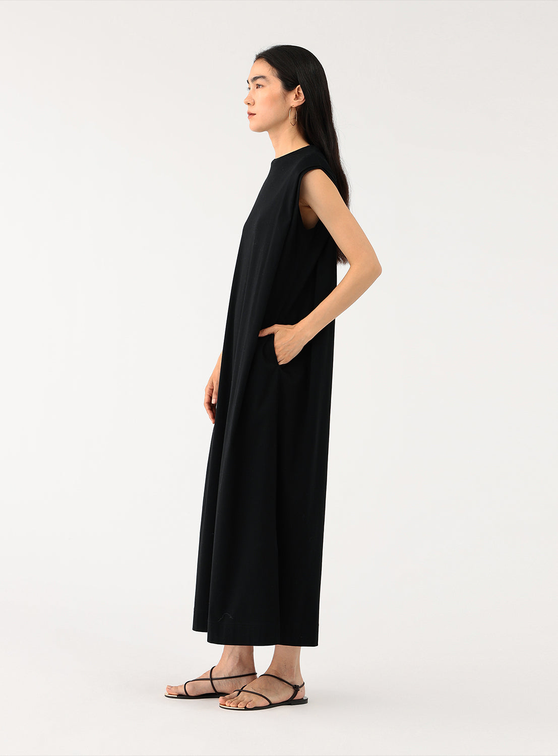Side view of a model wearing a black A-line midi dress, showing the relaxed drape and side pockets,