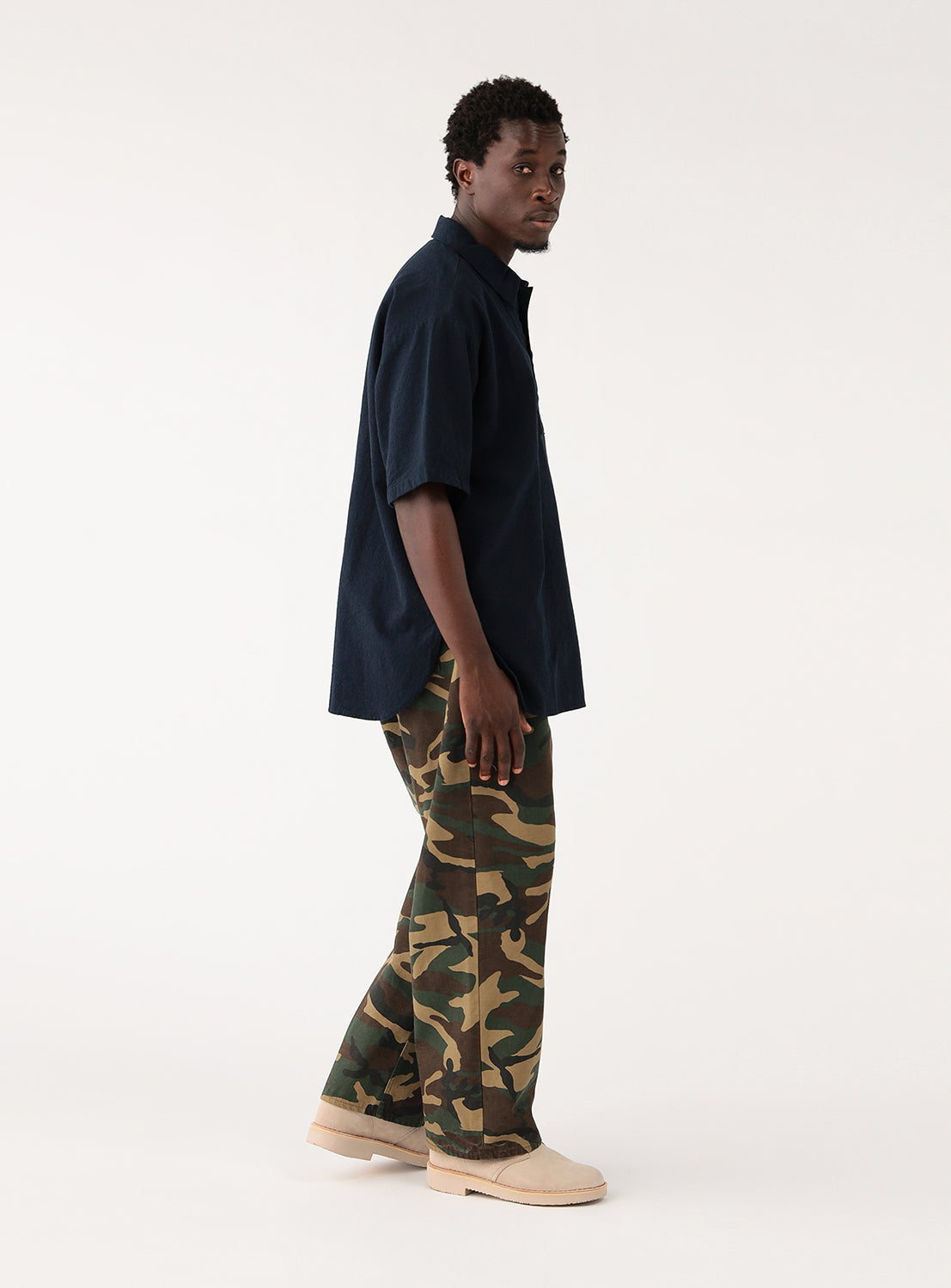 Model wearing navy blue open-collar shirt and camouflage pants, back view, showing the shirt's drape.