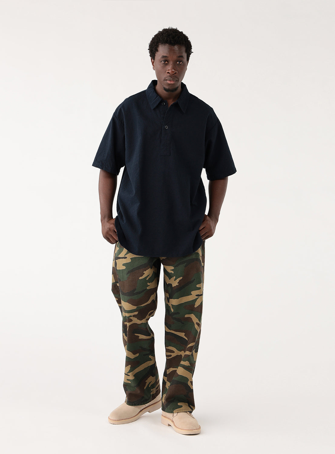 Model wearing navy blue open-collar shirt and camouflage pants, front view from below.
