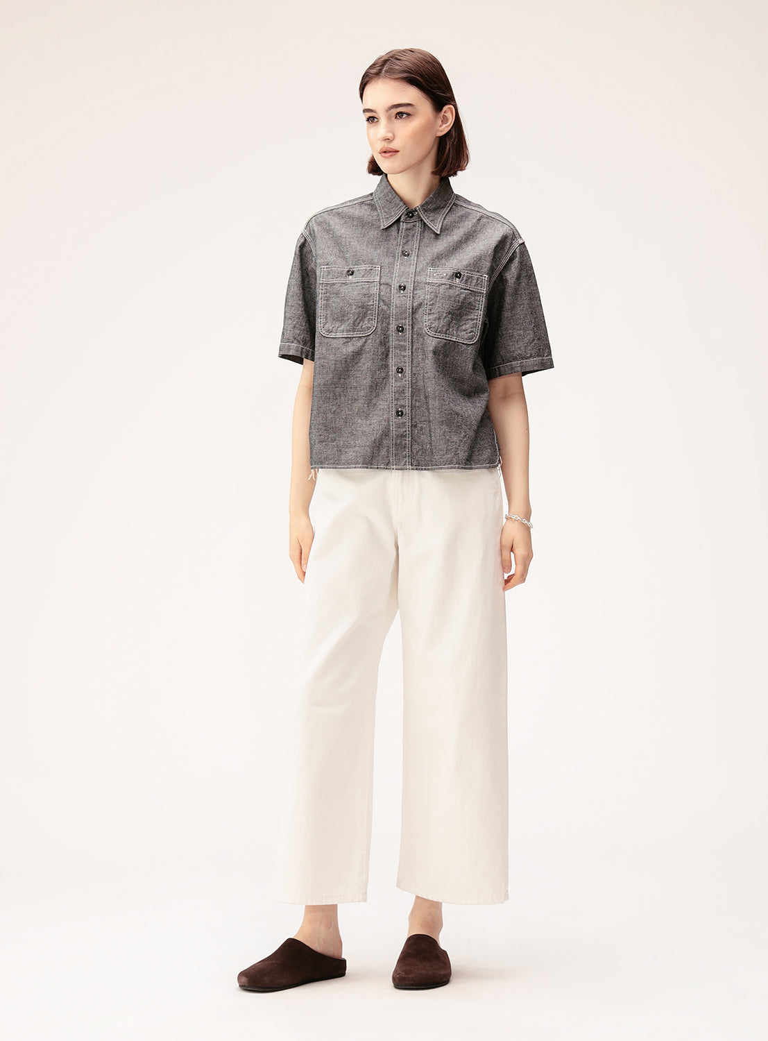 A person stands against a plain background wearing a short-sleeve gray button-up shirt, BEAMS BOY Straight Fit Wide Denim Pants, and dark brown slippers.