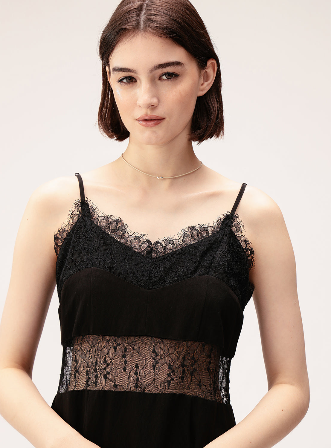 A woman with short brown hair wears the Ray BEAMS Lace Cut-Out Cami Dress, featuring thin straps and a sheer lace panel, styled with a delicate silver necklace as she stands against a plain light background.