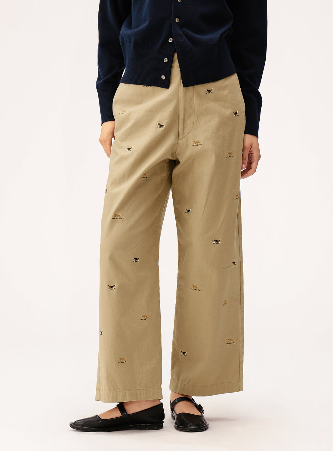 A person wearing BEAMS BOY Dog Embroidered Chino Pants, a navy cardigan, and black ballet flats stands against a plain light background.