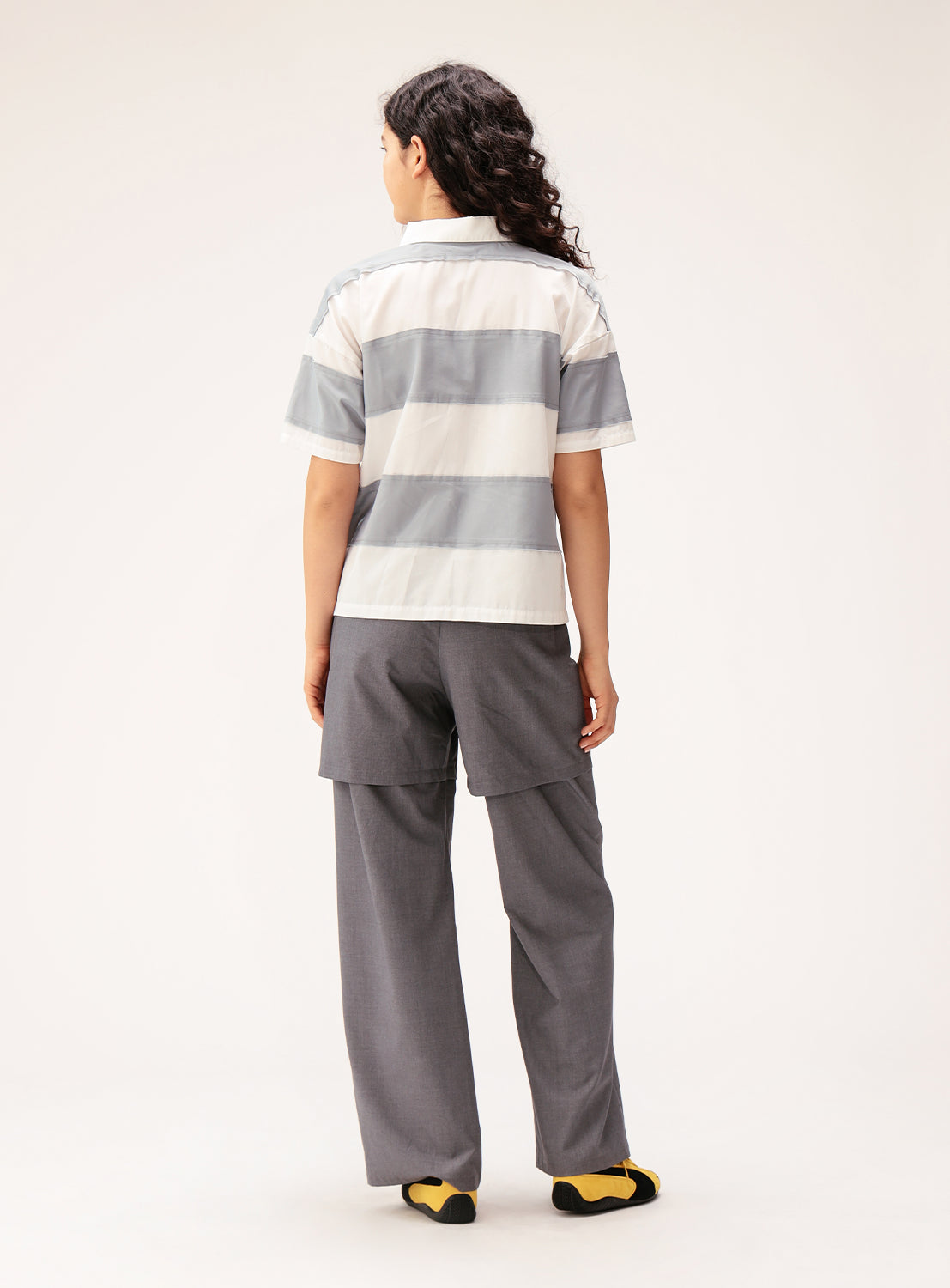 Person wearing a striped polo shirt and gray pants on a white background