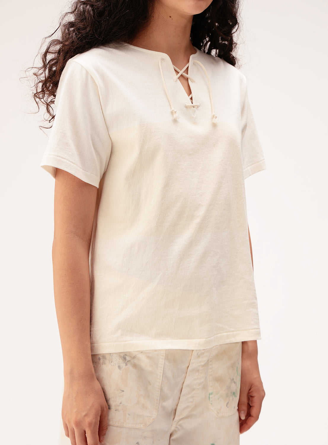 A person wearing the BEAMS BOY Wide Border Lace-Up Short Sleeve Top and light-colored pants with a subtle paint splatter pattern stands against a plain light background.