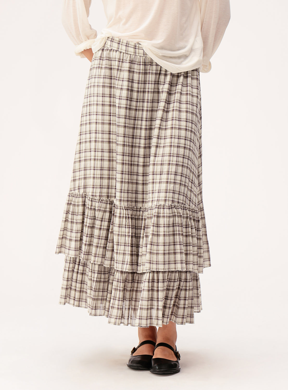 A person wearing a white long-sleeve top and the BEAMS BOY Check Tiered Skirt, featuring a check pattern and ankle-length design crafted from lightweight fabric, paired with black flat shoes, stands against a plain light background.