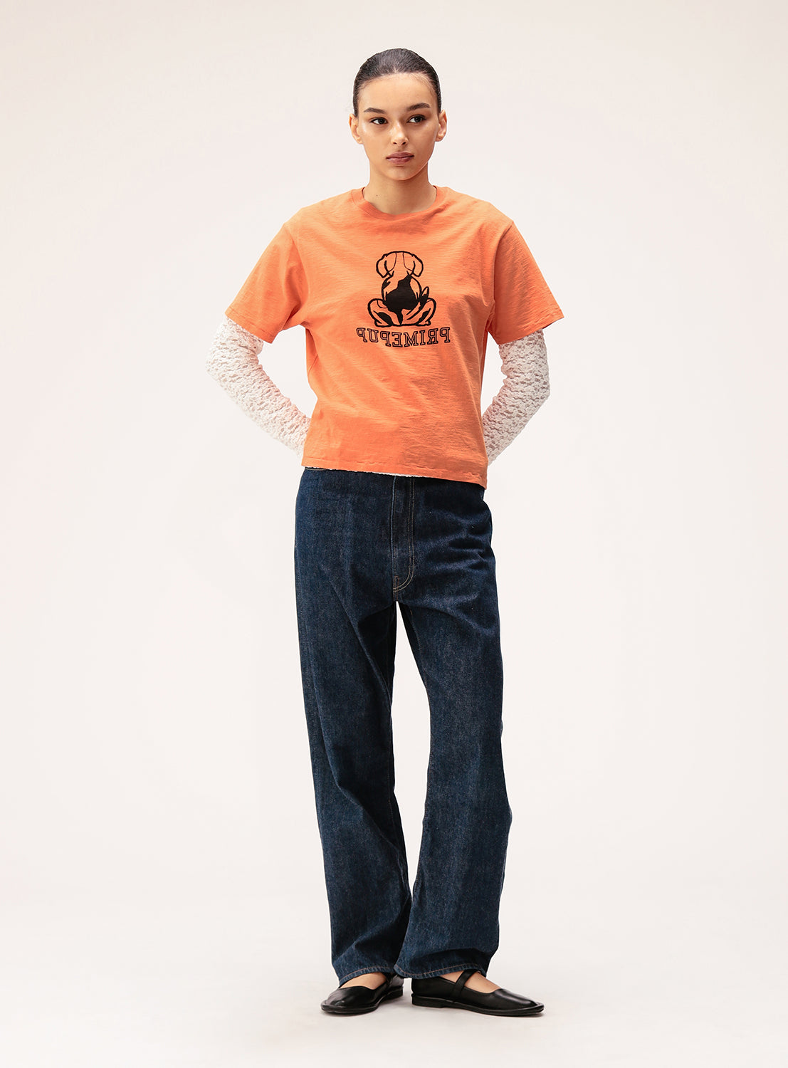 Person wearing an orange t-shirt with a graphic design and blue jeans on a white background