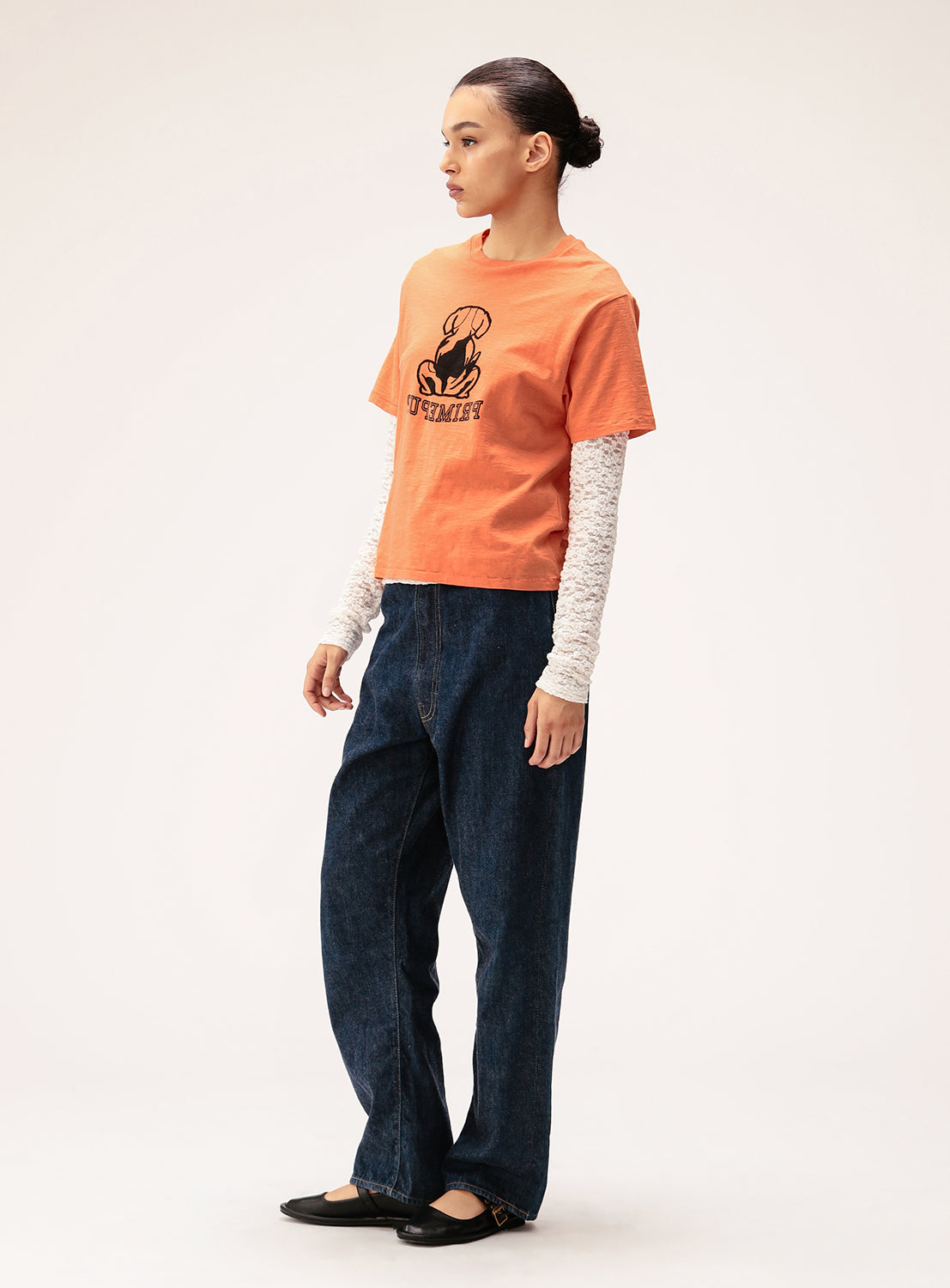 Person wearing an orange t-shirt with a graphic design and blue jeans on a white background