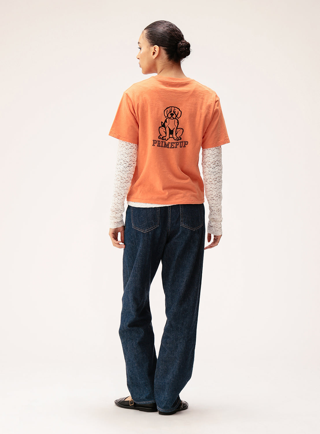 Person wearing an orange t-shirt with a logo and text, standing against a white background