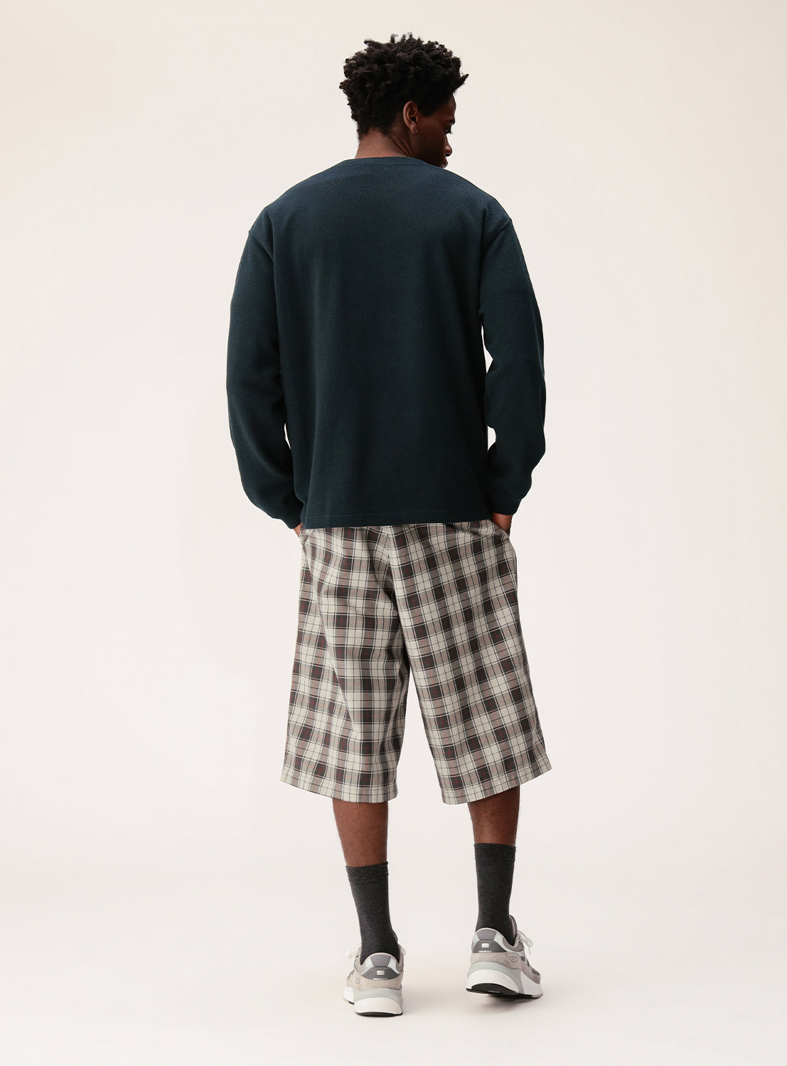A person faces away, wearing BEAMS Tartan Check Shorts, a dark long-sleeve shirt, dark socks, and sneakers against a plain light background.