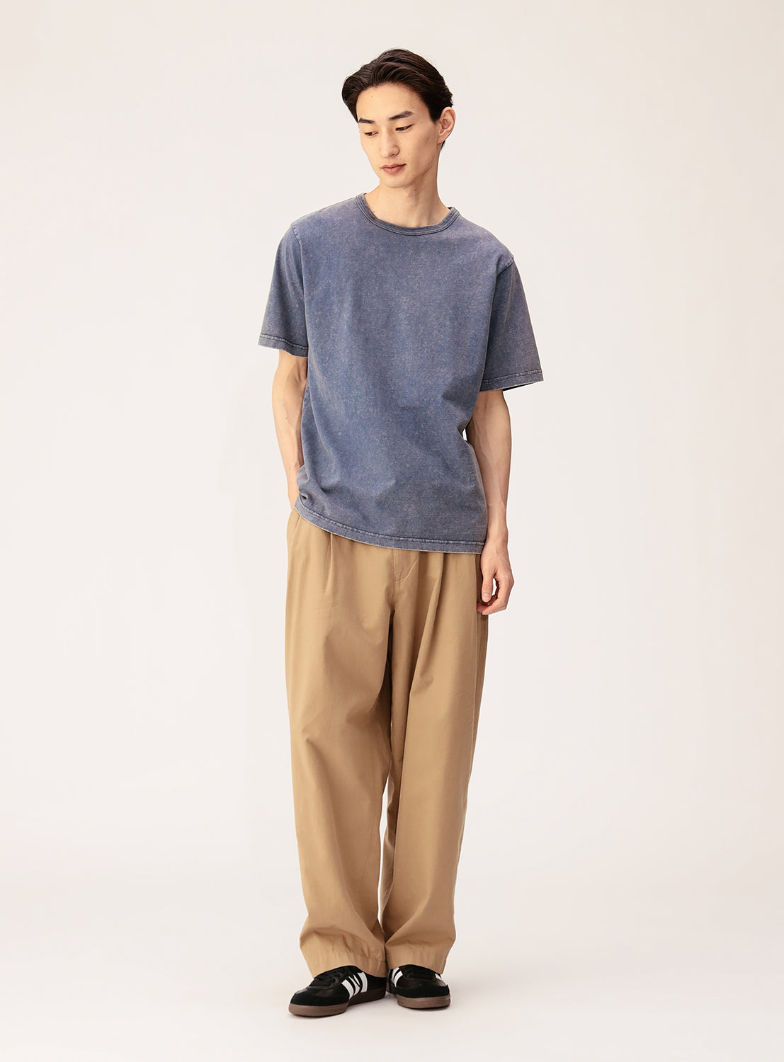 Against a plain light background, a person wears BEAMS' Ultra Faded Crew Neck T-Shirt in loose midweight cotton jersey, paired with wide beige pants and black sneakers with white stripes, hands in pockets and posture relaxed.