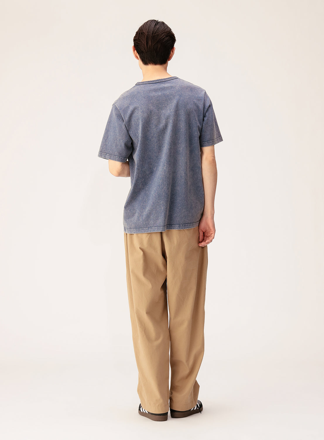 A person with short dark hair faces away, wearing the BEAMS Ultra Faded Crew Neck T-Shirt in midweight cotton jersey, paired with loose tan pants and sandals against a plain light background.