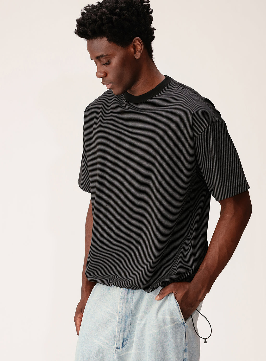 Man wearing a dark gray t-shirt and light blue jeans against a plain background