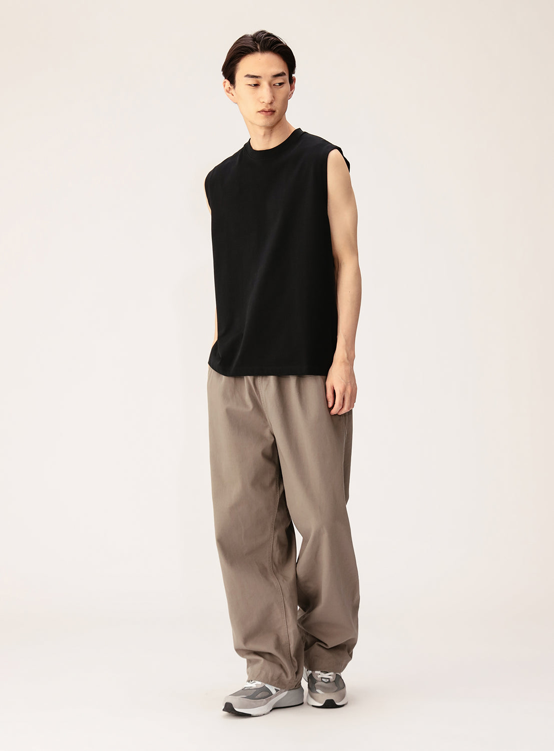 A person wearing the BEAMS Sleeveless Tank Top, loose beige pants, and gray sneakers stands against a plain light background, looking slightly to the side with a neutral expression.