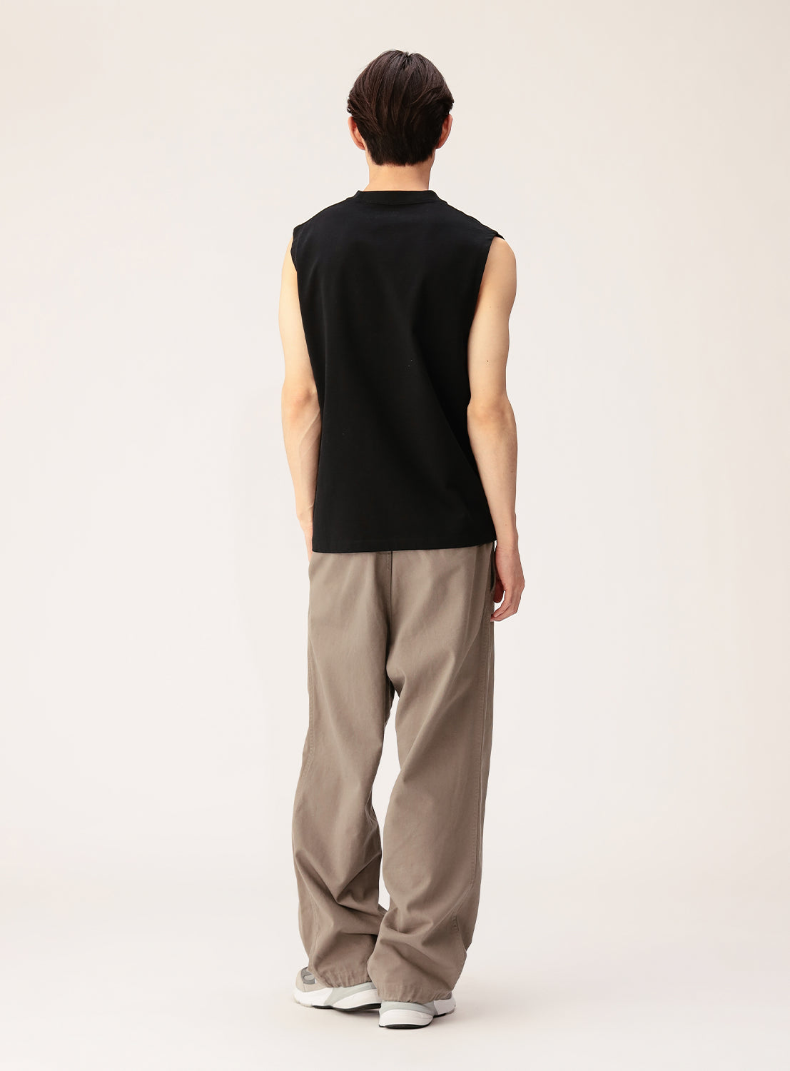 A person faces away from the camera, wearing a BEAMS Sleeveless Tank Top, loose beige pants with a relaxed fit, and white sneakers against a plain light background.